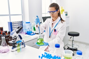 Young hispanic woman wearing scientist uniform using pipette and test tube working at laboratory