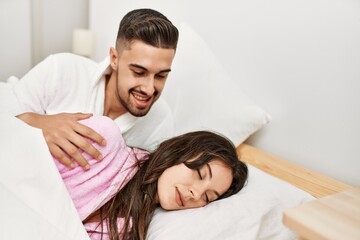 Obraz na płótnie Canvas Young hispanic man looking his sleepy girlfriend at bed.