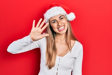 Beautiful hispanic woman wearing christmas hat showing and pointing up with fingers number five...
