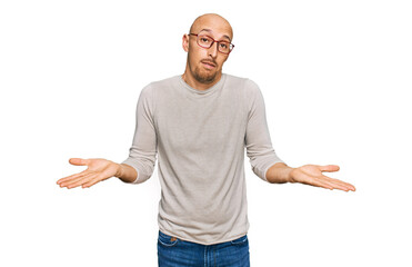 Bald man with beard wearing casual clothes and glasses clueless and confused expression with arms...