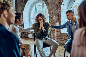 During group therapy sessions participants supporting crying desperate man, provide psychological assistance talking with him share mental pain try to help.