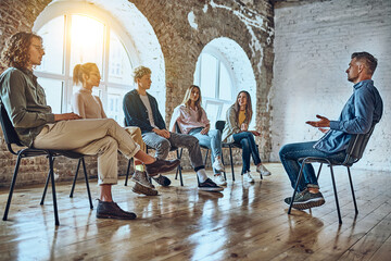 Positive people sit on the chairs take part in team building or therapy session, try to solve problems or do training exercise, focus on a man telling story share experience at group meeting concept.