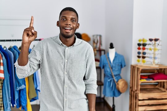 Young african american man working as manager at retail boutique pointing finger up with successful idea. exited and happy. number one.