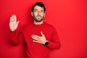 Handsome man with beard wearing casual red sweater swearing with hand on chest and open palm, making a loyalty promise oath