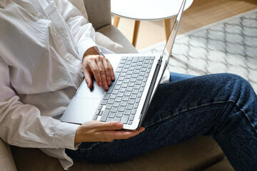 Girl works on the laptop on the couch at home or in hotels. Remote work. Office at home. Woman in the bedroom is typing on a laptop, distance learning for students, surfing the Internet