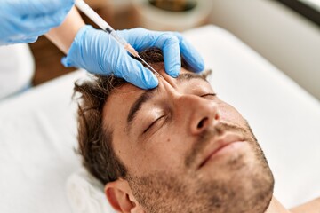 Fototapeta na wymiar Young hispanic man having facial anti-aging treatment at beauty center