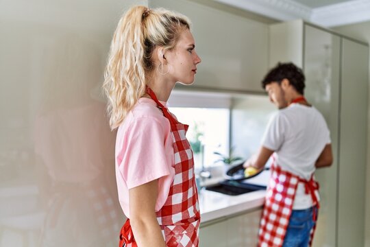 Young Caucasian Woman Wearing Apron And Husband Doing Housework Washing Dishes Looking To Side, Relax Profile Pose With Natural Face With Confident Smile.