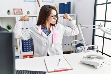 Obraz na płótnie Canvas Young doctor woman wearing doctor uniform and stethoscope at the clinic showing arms muscles smiling proud. fitness concept.