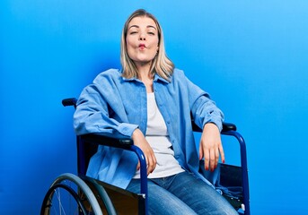 Beautiful caucasian woman sitting on wheelchair making fish face with lips, crazy and comical gesture. funny expression.