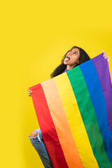 Mujer afroamericana haciendo gestos en fondo amarillo con la bandera de la diversidad en sus manos