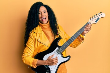 Middle age african american woman playing electric guitar smiling and laughing hard out loud...