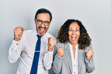 Middle age couple of hispanic woman and man wearing business office uniform celebrating surprised and amazed for success with arms raised and open eyes. winner concept.