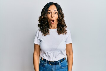 Middle age hispanic woman wearing casual white t shirt afraid and shocked with surprise expression, fear and excited face.