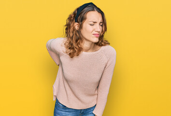 Beautiful young caucasian woman wearing casual sweater suffering of backache, touching back with...