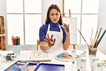 Young brunette woman at art studio with painted hands disgusted expression, displeased and fearful doing disgust face because aversion reaction. with hands raised