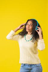 Hermosa mujer afroamericana con audífonos escuchando música en fondo amarillo de estudio viendo a cámara