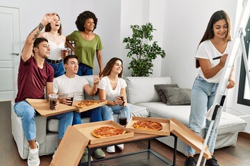 Group of young friends eating pizza and playing draw game at home.