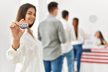 Group of young american voter people putting vote in ballot. Woman smiling happy and holding i voted badge at electoral center.