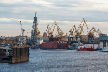 Naklejka premium Ship building plant. Large cranes build various vessels. Dry dock. Cloudy sky. Pier with ships. Creation concept.