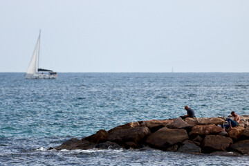People on the rocks with sailboat behind