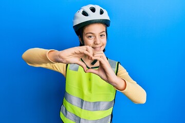 Beautiful brunette little girl wearing bike helmet and reflective vest smiling in love doing heart symbol shape with hands. romantic concept.