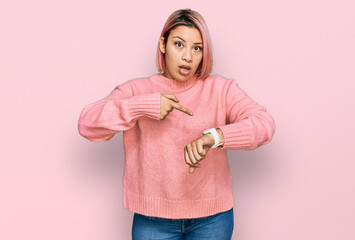 Hispanic woman with pink hair wearing casual winter sweater in hurry pointing to watch time, impatience, upset and angry for deadline delay