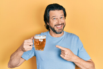 Middle age caucasian man drinking a jar of beer smiling happy pointing with hand and finger