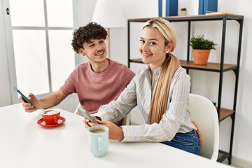 Young couple using smartphone and drinking coffee at home.