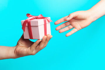 Male hand giving a gift box to female hand on blue background.