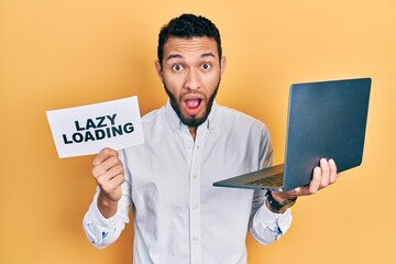 Hispanic man with beard working using computer laptop holding lazy loading banner afraid and shocked with surprise and amazed expression, fear and excited face.