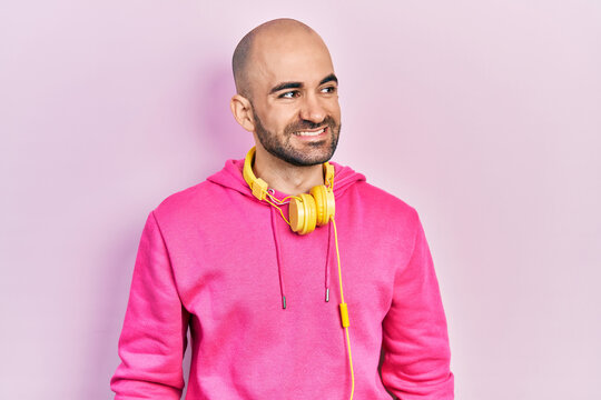 Young bald man wearing gym clothes and using headphones looking away to side with smile on face, natural expression. laughing confident.