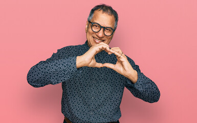 Middle age indian man wearing casual clothes and glasses smiling in love doing heart symbol shape...
