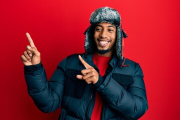Young african american man with beard wearing winter hat and coat smiling and looking at the camera...