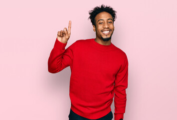 Young african american man with beard wearing casual winter sweater showing and pointing up with finger number one while smiling confident and happy.