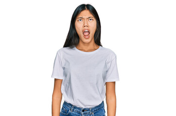 Beautiful young asian woman wearing casual white t shirt angry and mad screaming frustrated and furious, shouting with anger. rage and aggressive concept.