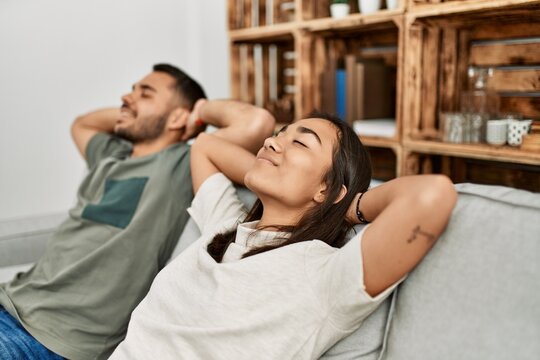 Young latin couple resting with head on hands sitting on the sofa at home.