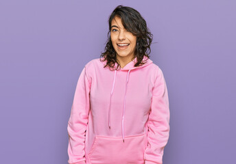 Young hispanic woman wearing casual sweatshirt winking looking at the camera with sexy expression,...