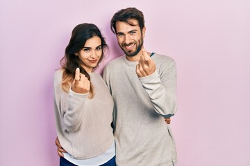 Young hispanic couple wearing casual clothes beckoning come here gesture with hand inviting welcoming happy and smiling