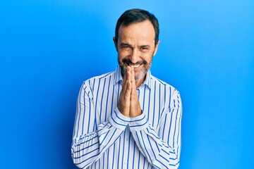 Middle age hispanic man wearing casual clothes praying with hands together asking for forgiveness smiling confident.