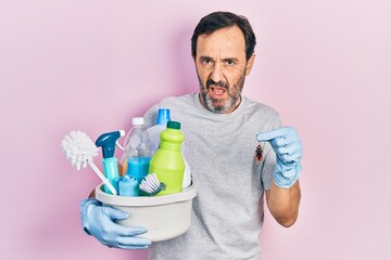 Middle age hispanic man holding cleaning products holding cockroach clueless and confused...