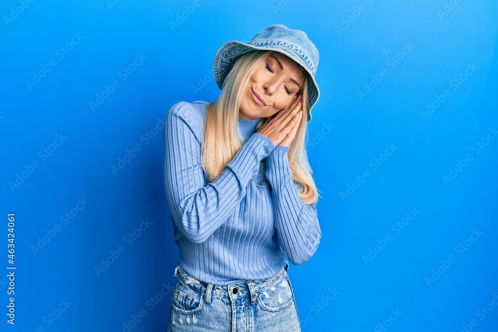 Poster young blonde woman wearing casual denim hat sleeping tired dreaming and posing with hands together w