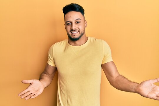 Young arab man wearing casual clothes clueless and confused expression with arms and hands raised. doubt concept.