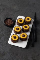 Pumpkin cream dessert with chocolate sprinkles and filling in the form of sushi rolls on a ceramic plate on a dark gray background top view