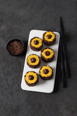 Sweet creamy pumpkin sushi rolls with chocolate sprinkles and filling on a ceramic plate on a dark...