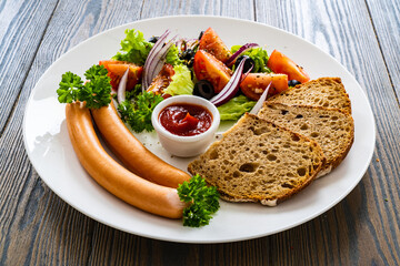Breakfast - boiled sausages, bread and fresh vegetables served on wooden table
