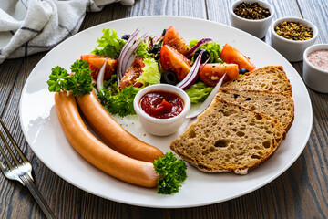 Breakfast - boiled sausages, bread and fresh vegetables served on wooden table
