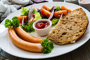 Breakfast - boiled sausages, bread and fresh vegetables served on wooden table
