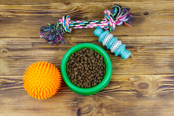 Obraz na płótnie Canvas Dog toys and feed for dogs in green plastic bowl on wooden background. Top view. Dog care concept