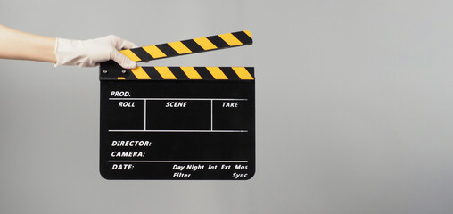 Hand is holding yellow with black clapper board color  and wear medical glove on grey background.