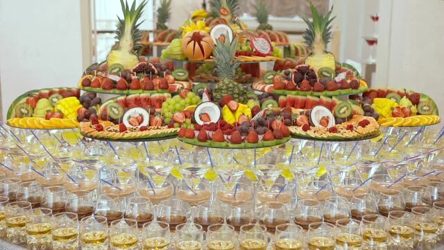 Festive buffet with exotic fruits and alcoholic beverages. Fresh ripe sliced fruit on trays and in front are rows of glasses with expensive and delicious alcoholic beverages. Holiday.